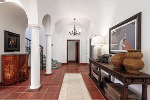 Un vaste hall d’entrée avec des colonnes blanches, un lustre, une console en bois agrémentée d’objets décoratifs et un tableau encadré au mur.