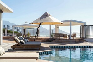 Un espace piscine avec des chaises longues, une pergola et une vue sur l’océan.