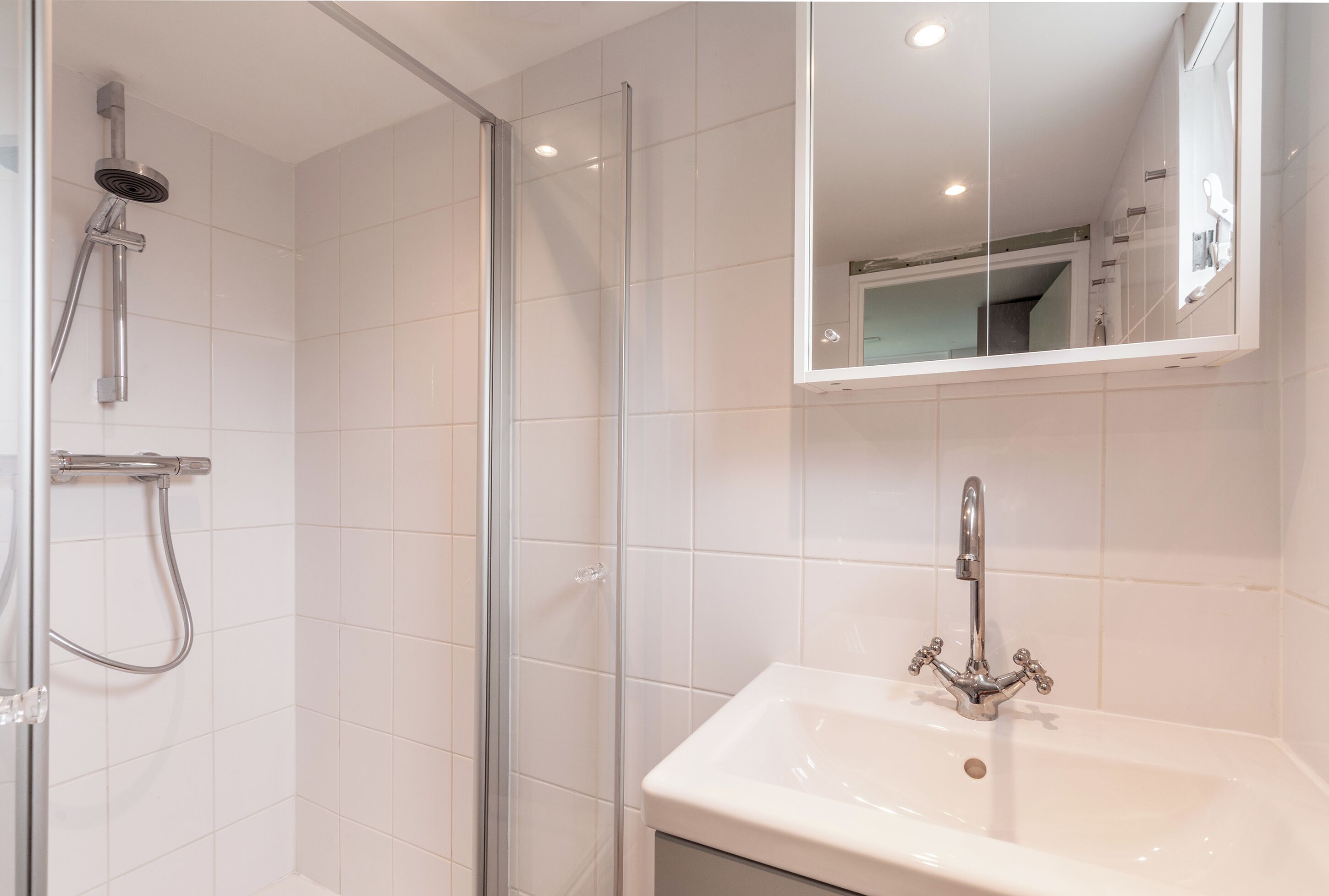 A bathroom with a glass shower enclosure, a white sink with a chrome faucet, and a mirror above the sink.