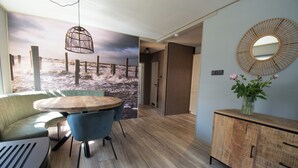 Un salon moderne avec une table ronde en bois, des chaises bleues, un canapé, un meuble en bois et une fresque murale représentant une scène de plage.