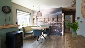 Une pièce chaleureuse avec une table en bois, des chaises, un petit poêle et une grande fresque murale représentant une scène de plage.