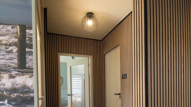 Un couloir doté d’un plancher en bois, d’une porte avec un panneau de verre et de lambris verticaux en bois sur les murs.