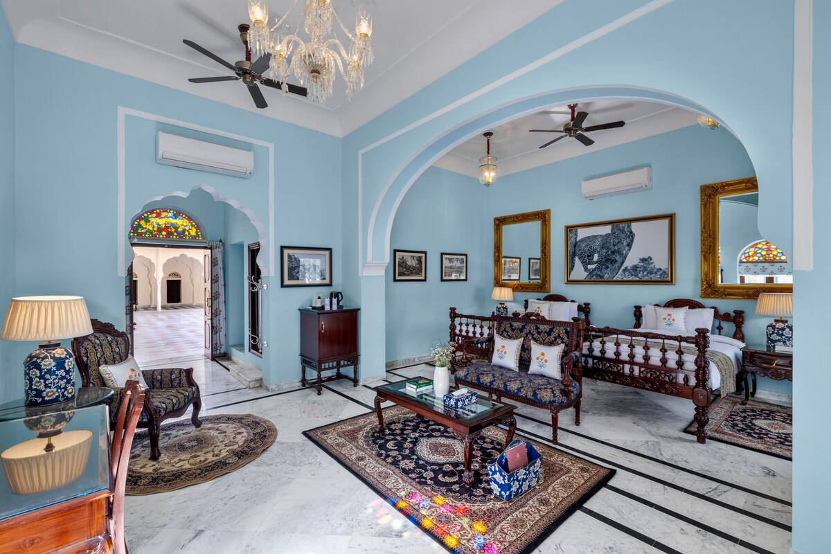 A room with a chandelier, ceiling fans, a bed, a sofa, a coffee table, and a rug.