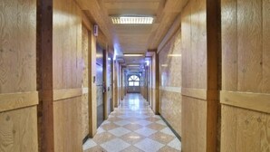 Um corredor longo com paredes de madeira e chão xadrez, que termina numa janela.