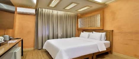 Habitación de hotel con cama, escritorio con computadora, unidad de aire acondicionado y ventana con cortinas.
