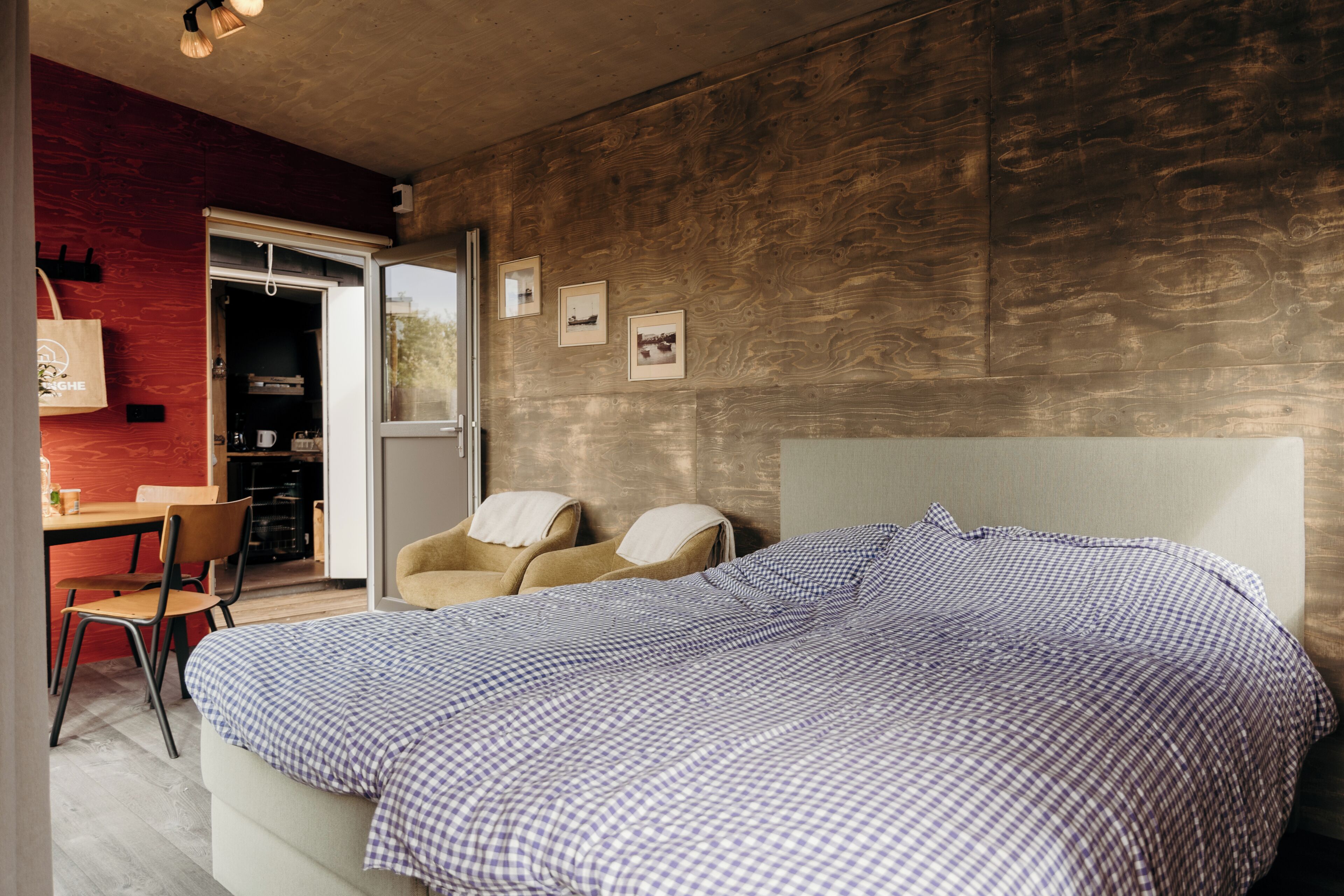 A bedroom with a large bed, a chair, a desk, and a view of the outside.