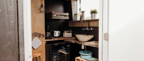 Cocina compacta con horno empotrado, estantes de madera, lámpara colgante y ventana.