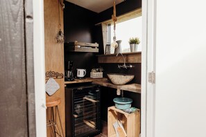 Eine kleine Küche mit eingebautem Backofen, Holzregalen, einer Hängelampe und einem Fenster.