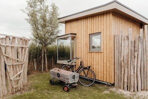 Eine Holzhütte mit einem Fahrrad und einem Wagen, umgeben von einem Holzzaun und Vegetation.