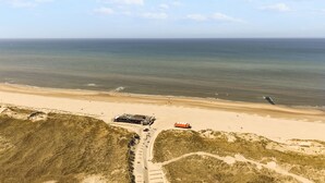 An aerial view of a coastal area with a beach, a road leading to a building with a red roof, and the ocean in the background. - A modernly furnished vacation rental with a view of the dunes of Groote Keeten. (Callantsoog)