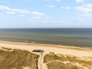 Ein Luftbild einer Küstenlandschaft mit Strand, einer Straße, die zu einem Gebäude mit rotem Dach führt, und dem Ozean im Hintergrund.