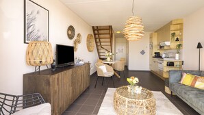 A modern living room with a sofa, a coffee table, a TV, and a dining area with chairs and a table. - A modernly furnished vacation rental with a view of the dunes of Groote Keeten. (Callantsoog)