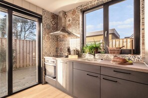 A modern kitchen with a sliding glass door, a built-in oven, and a large window. - Zand Vacation Home – Luxury, Peace, and Space on the Coast (Julianadorp)