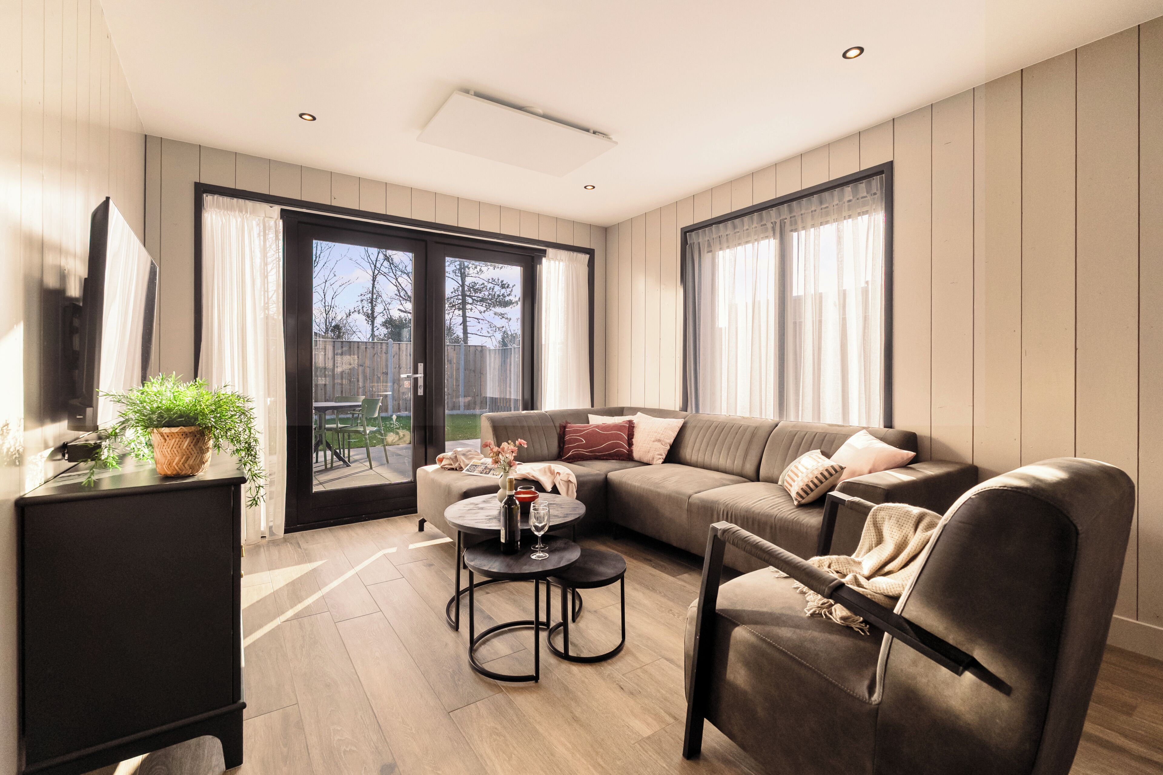 Un salon moderne avec un canapé, une table basse et un fauteuil. Une porte-fenêtre coulissante donne accès à un espace extérieur.