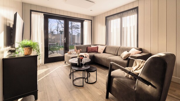 En moderne stue med en sofa, et sofabord og en lænestol. Der er en skydedør af glas, som fører til et udendørs område.