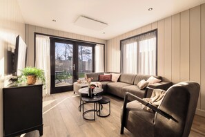 A modern living room with a sofa, a coffee table, and a chair. There is a sliding glass door leading to an outdoor area. - Holiday Home Zee Luxury, peace and space by the coast (Julianadorp)