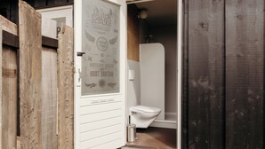 A wooden exterior with a white door leading to a bathroom featuring a toilet and a shower. - Unique accommodation (Callantsoog)