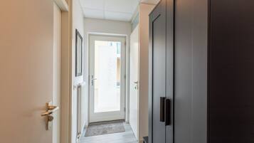 Een gang met een deur die leidt naar een lichte kamer, een donkere deur en een vloer in een lichte tint.