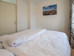 A bedroom with a bed, a door, and a wall-mounted picture.