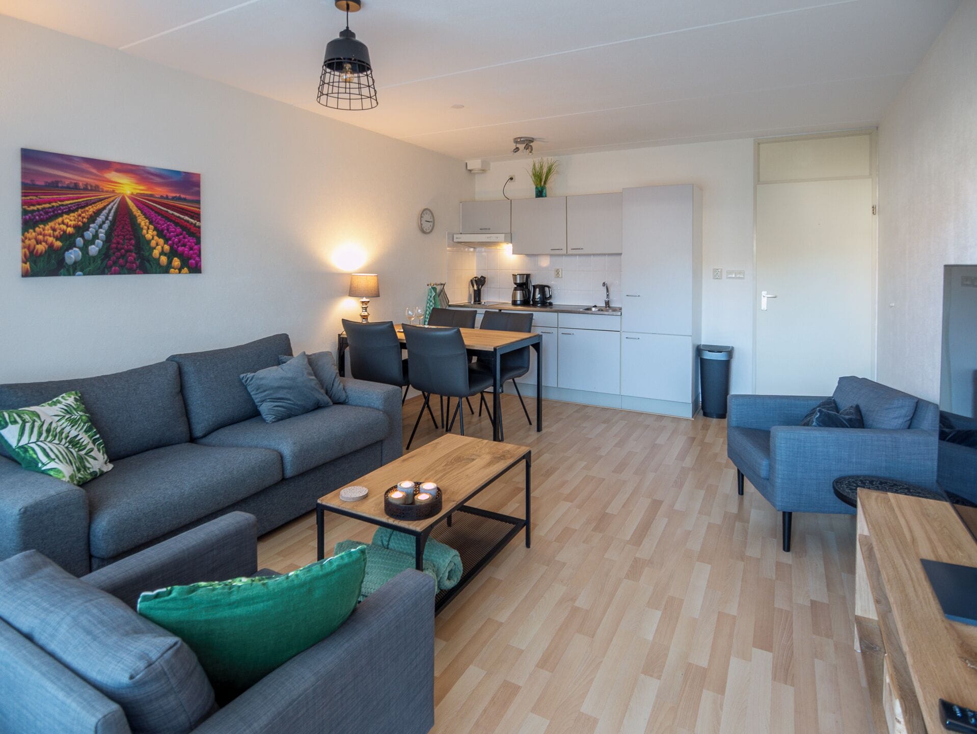 Una sala de estar moderna con sofá, mesa de centro y sillas, un comedor con mesa y sillas, y una cocina con gabinetes y un lavamanos.