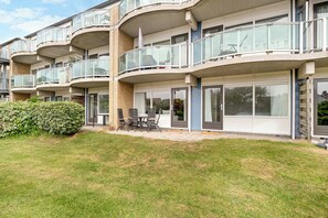 Ein mehrgeschossiges Wohngebäude mit Balkonen, einer Terrasse mit Gartenmöbeln und einem gepflegten Rasen.