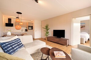 Ein modernes Wohnzimmer mit einer Couch, einem Couchtisch, einem Fernseher und einem Essbereich mit Tisch und Stühlen.