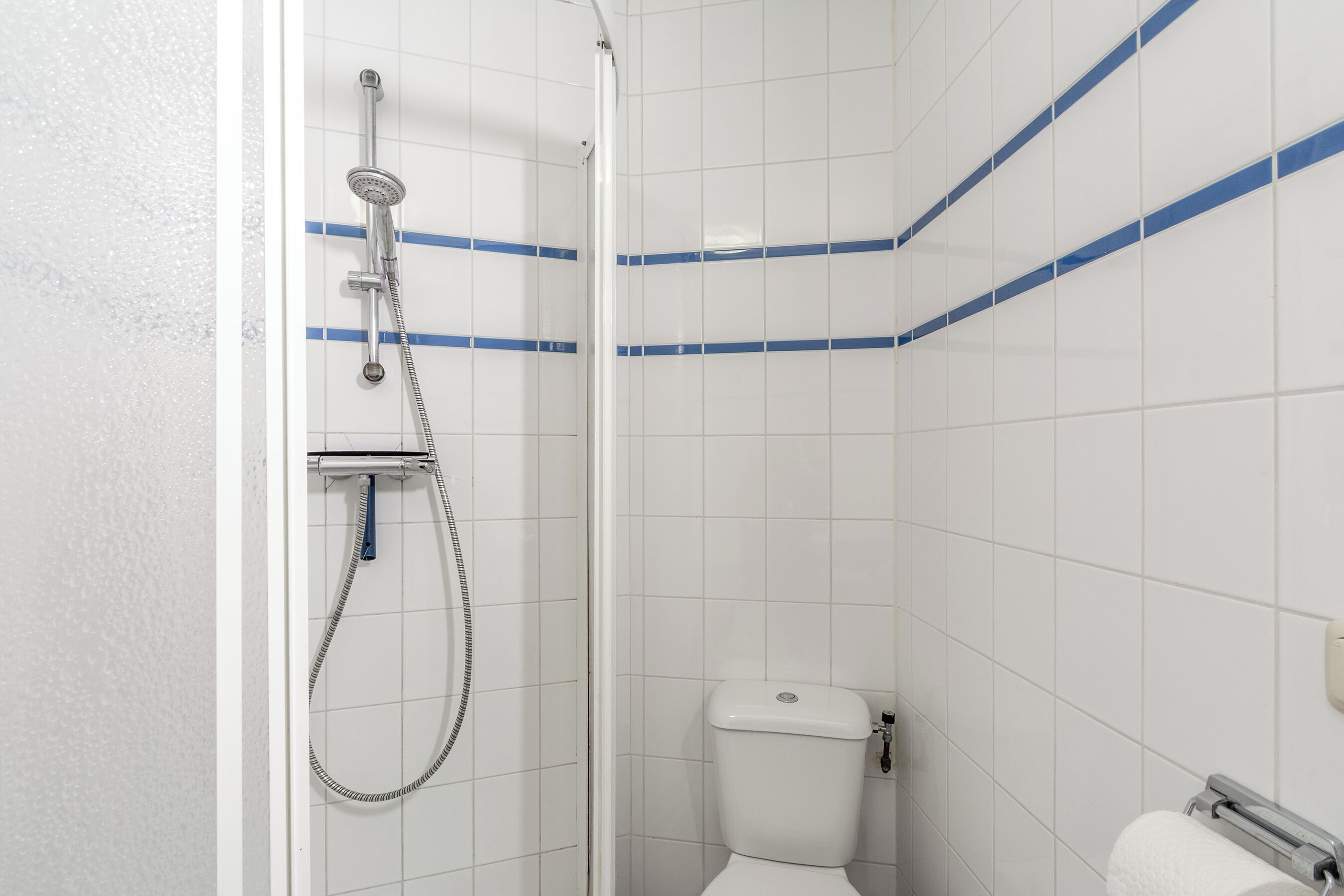 A bathroom with white tiles, a shower, a toilet, and a towel rack.