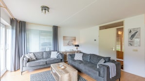 Ein modernes Wohnzimmer mit zwei grauen Sofas, einem Holztisch und einem gemusterten Teppich.