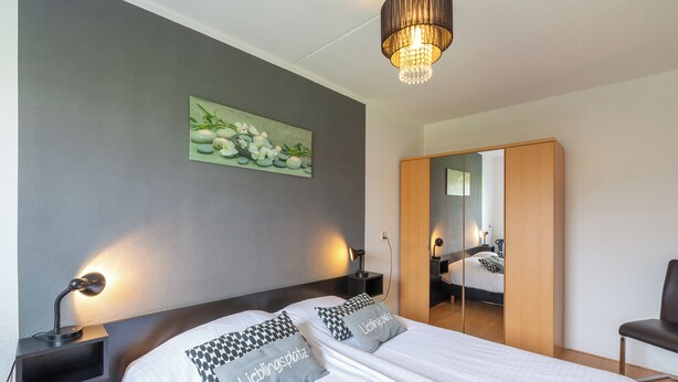 Ein Hotelzimmer mit Bett, Nachttischlampen, einem Spiegel, einem Kleiderschrank und einem Bild an der Wand.