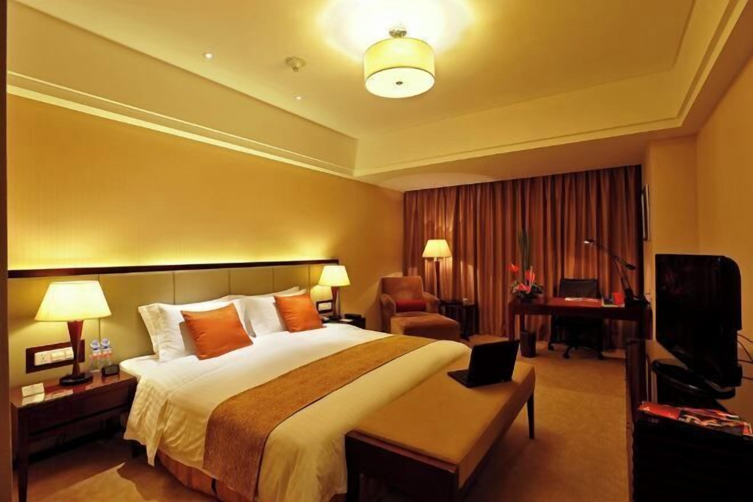 Habitación de hotel con una cama grande, lámparas de noche, un escritorio con una computadora, un televisor y una cortina.