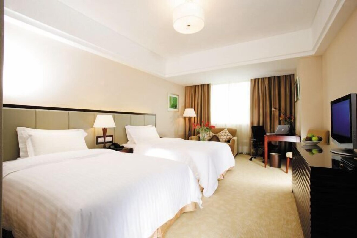 A hotel room with two beds, a desk, a television, and a window with curtains.