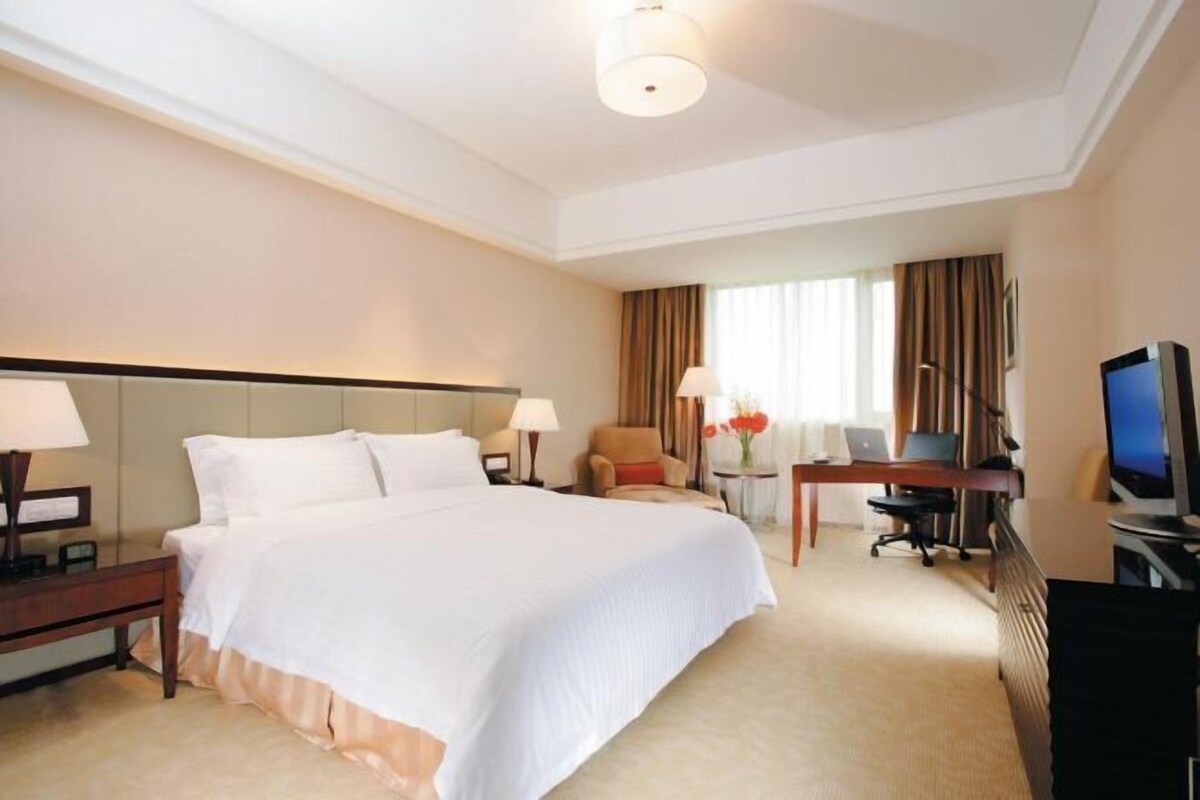 A hotel room with a large bed, a desk, a chair, a television, and a lamp.
