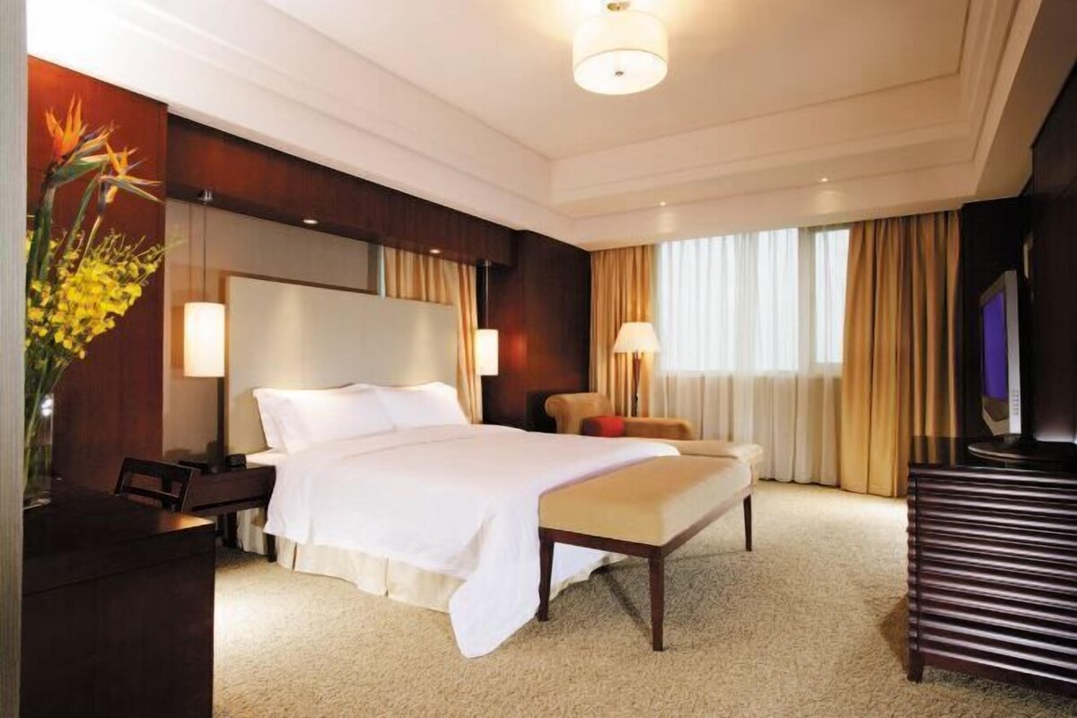 A hotel room with a bed, bedside table, lamp, and a television.
