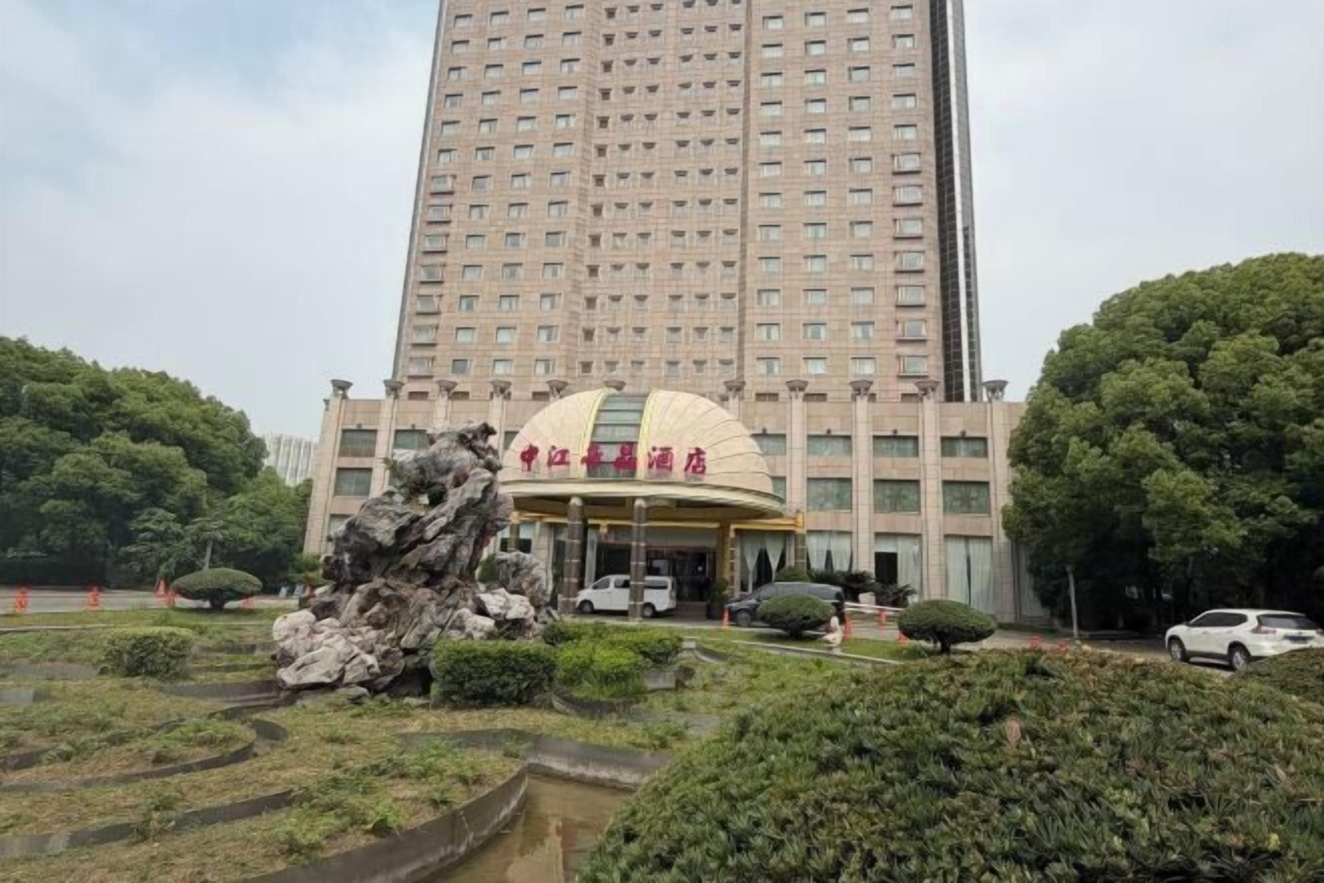 Un hotel con un edificio grande y un área de entrada ajardinada.