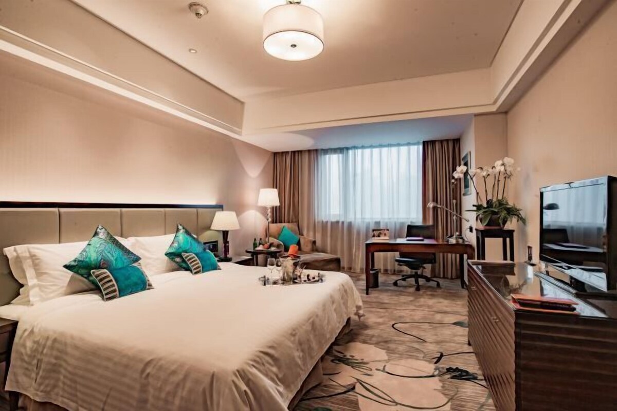 A hotel room with a large bed, a desk, a chair, a television, and a window with curtains.