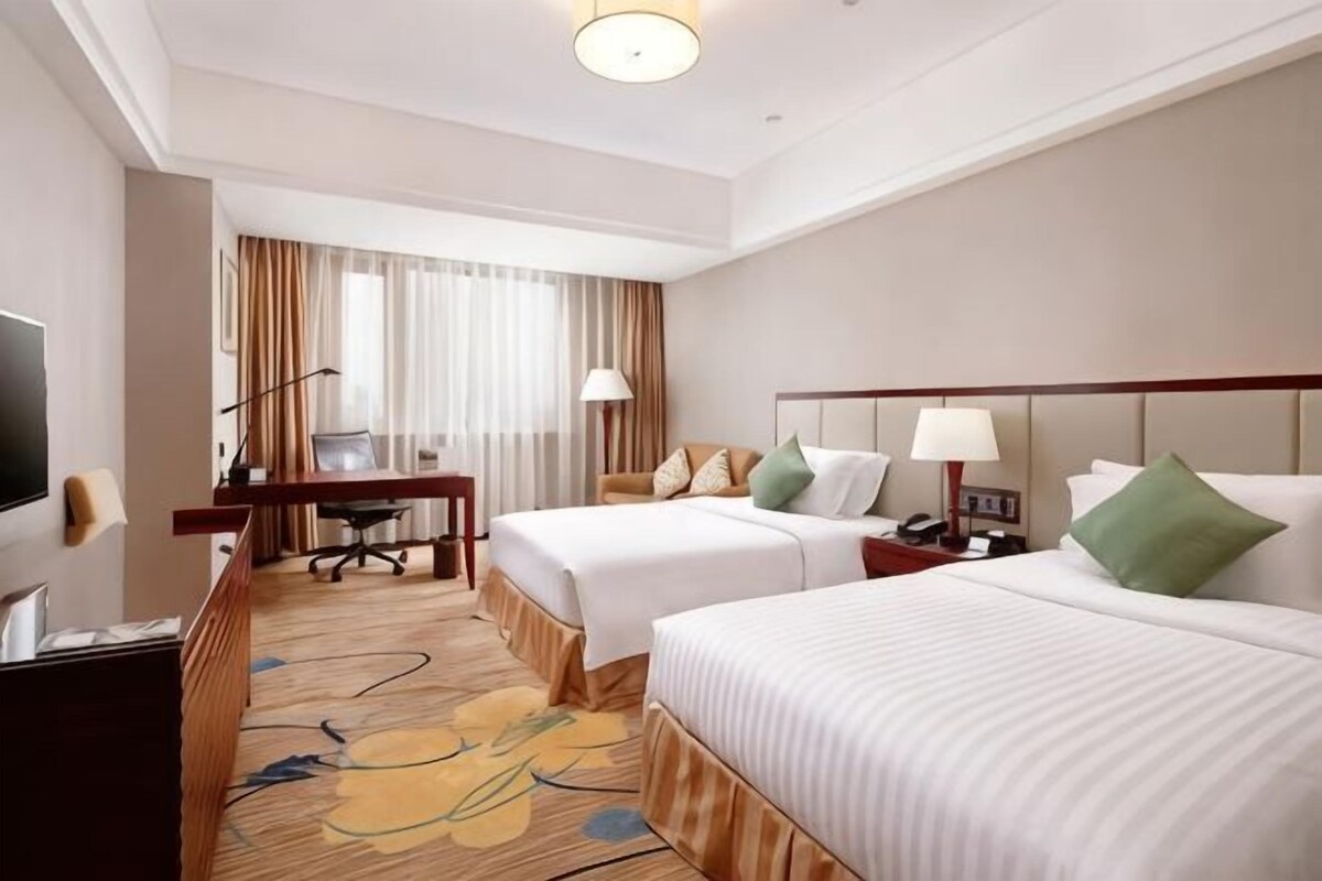 A hotel room with two beds, a desk, a TV, and a window with curtains.