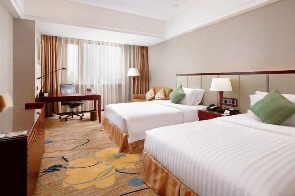 A hotel room with two beds, a desk, a chair, and a large window with curtains.