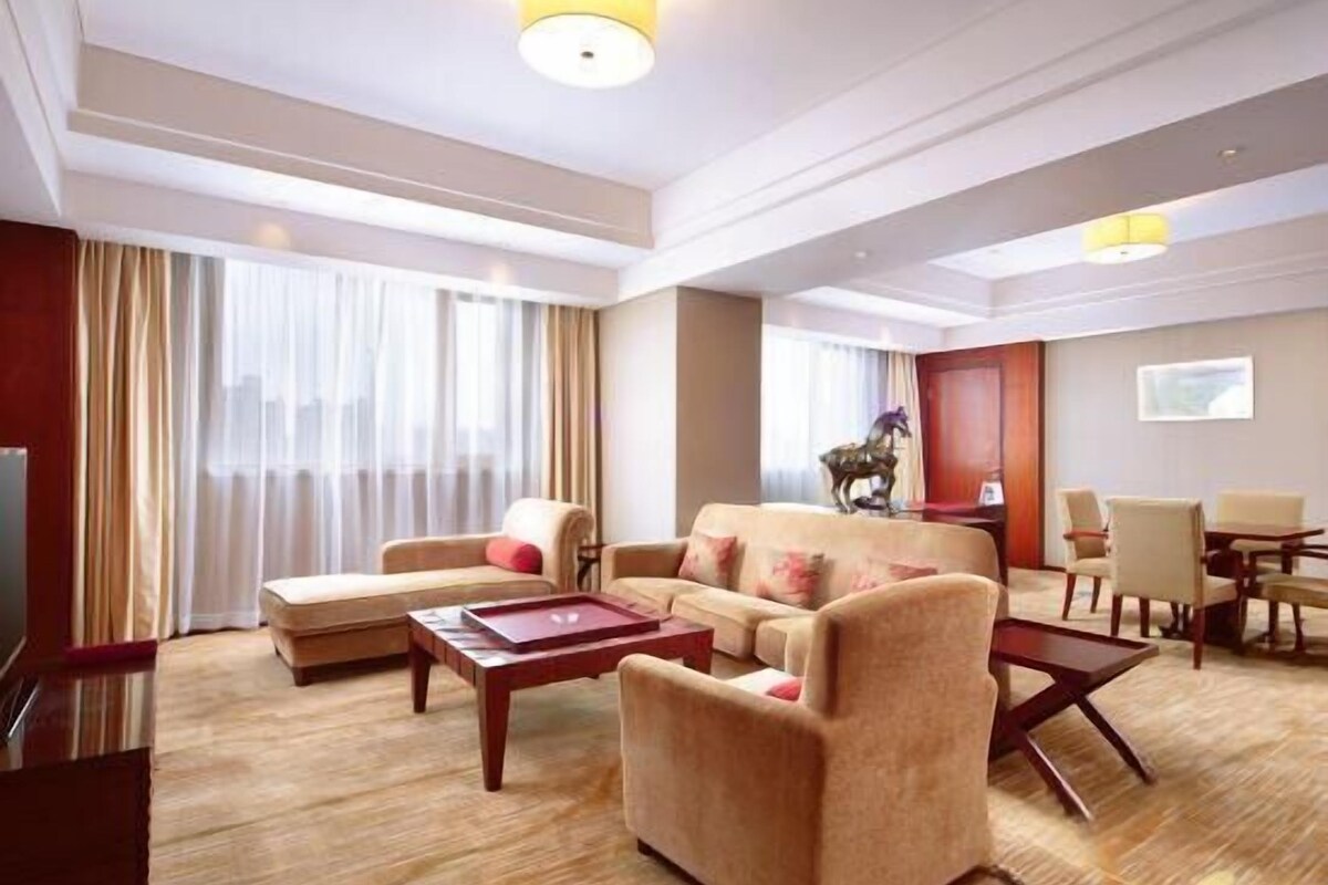 A hotel room with a sofa set, a coffee table, a TV, and a dining area.