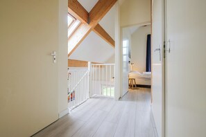 Ein Flur mit Holzbalken, einem weißen Geländer und einem Bett im Hintergrund.