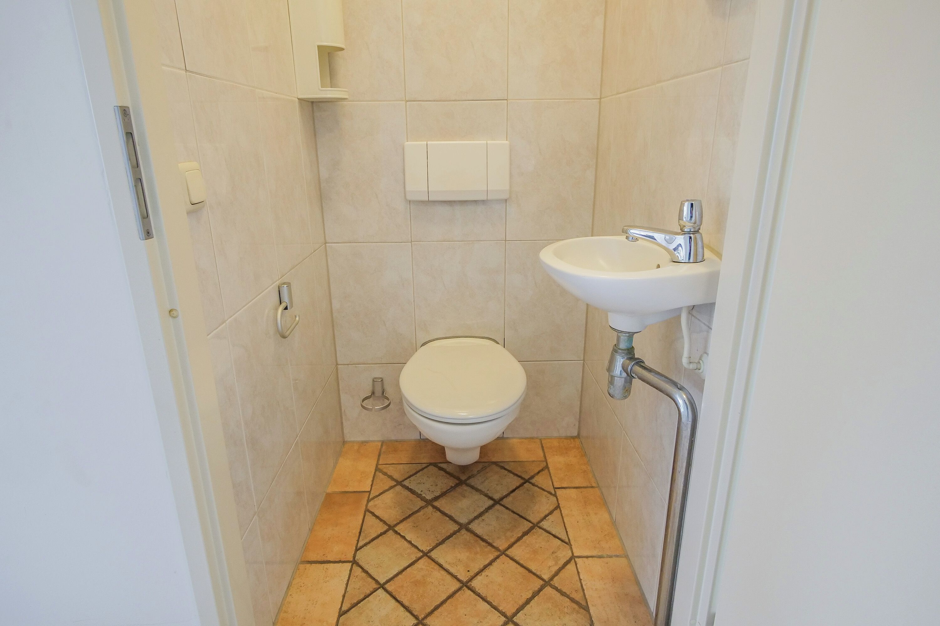 A small bathroom with a toilet, sink, and a tiled floor.