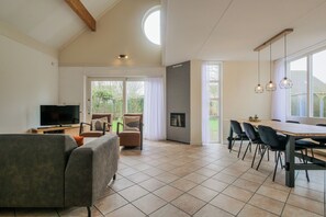 Ein großzügiger Wohnbereich mit Fernseher, Sofa, Esstisch, Stühlen und Kamin.