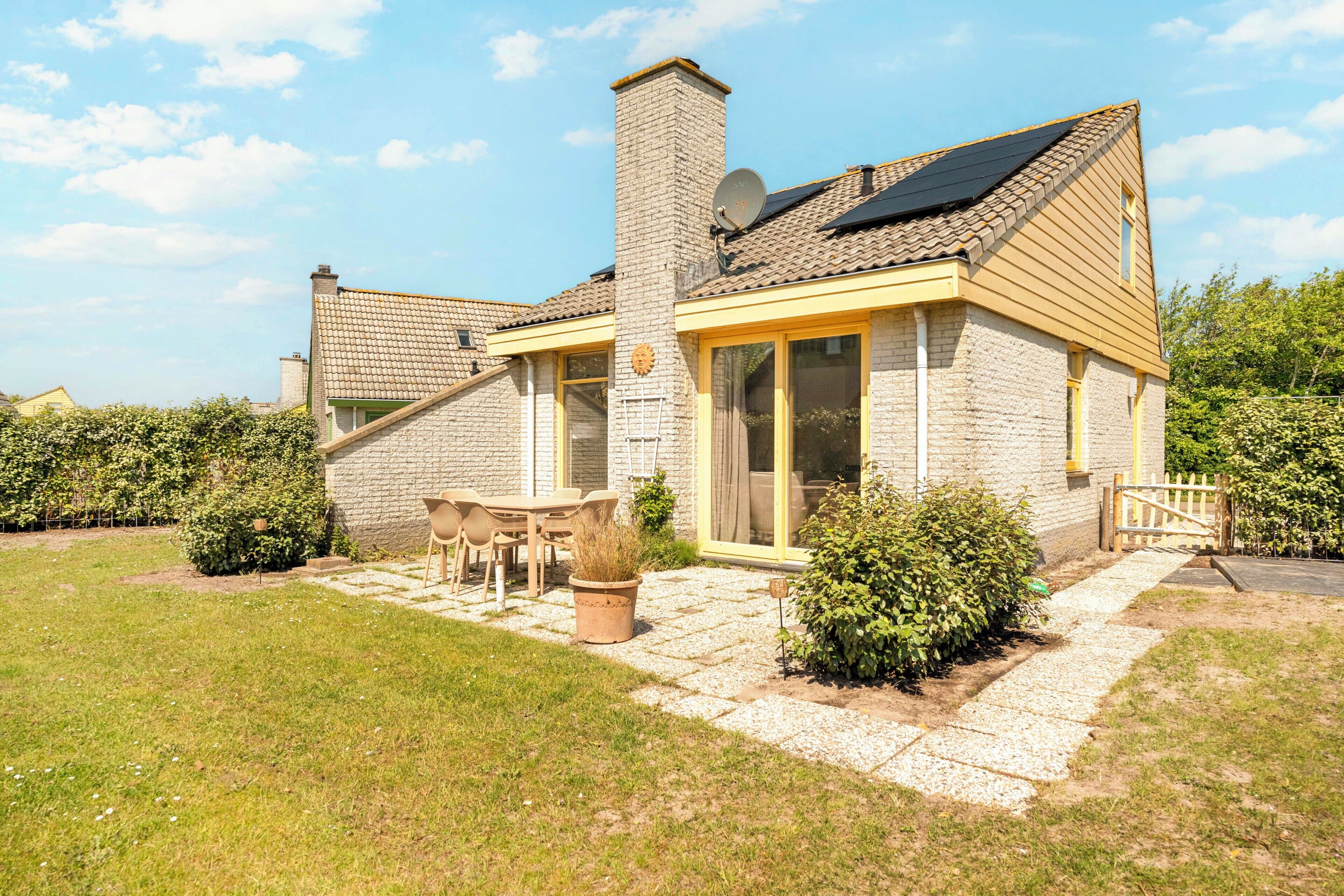 A two-story house with a brick exterior, a chimney, a patio with a table and chairs, and a garden.