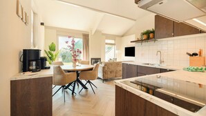 A modern kitchen with a dining area, wooden cabinets, a built-in oven, and a large window. - This beautiful detached vacation home in Julianadorp aan Zee is fully equipped with all modern conveniences. (Julianadorp)