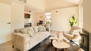 A living room with a sofa, armchair, round coffee table, and a fireplace. - This beautiful detached vacation home in Julianadorp aan Zee is fully equipped with all modern conveniences. (Julianadorp)