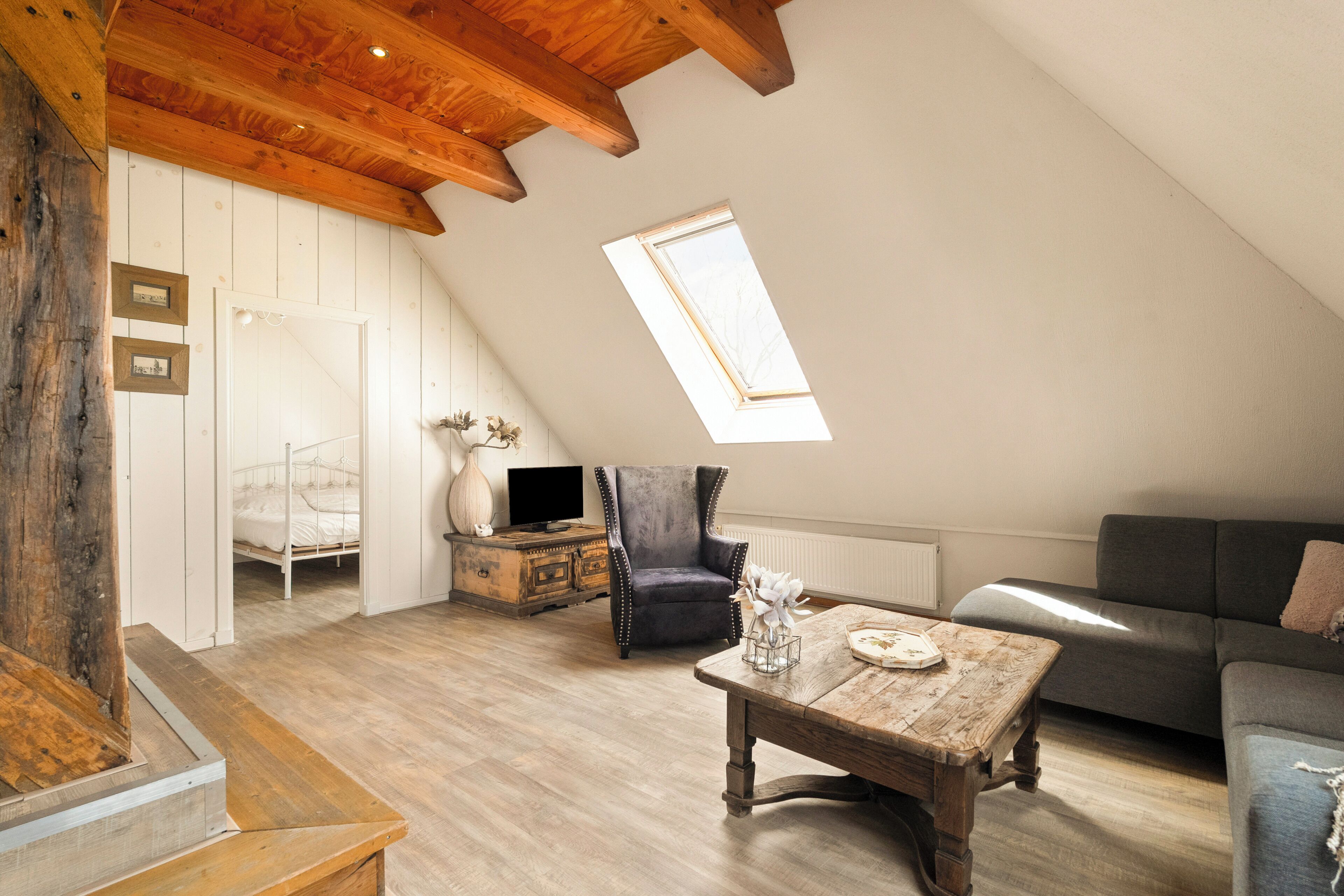 A loft-style room with a sloped ceiling, a wooden table, a sofa, a chair, and a television on a dresser.