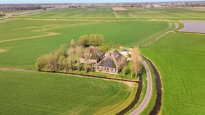 Luchtbeeld van een landgoed met een groot huis, omgeven door uitgestrekte groene velden en een kronkelende weg.