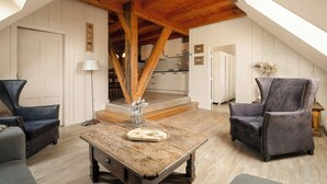 Een kamer met een houten plafond, een eettafel, twee stoelen en een keuken op de achtergrond.