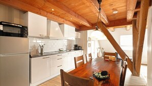 Een keuken met witte kastjes, een houten eettafel en een hangende lamp.