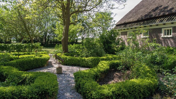Een tuinpad dat leidt naar een traditioneel gebouw met rieten dak.