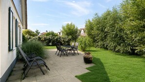 Eine Terrasse mit Tisch und Stühlen, einem Blumentopf und einem gepflegten Rasen.